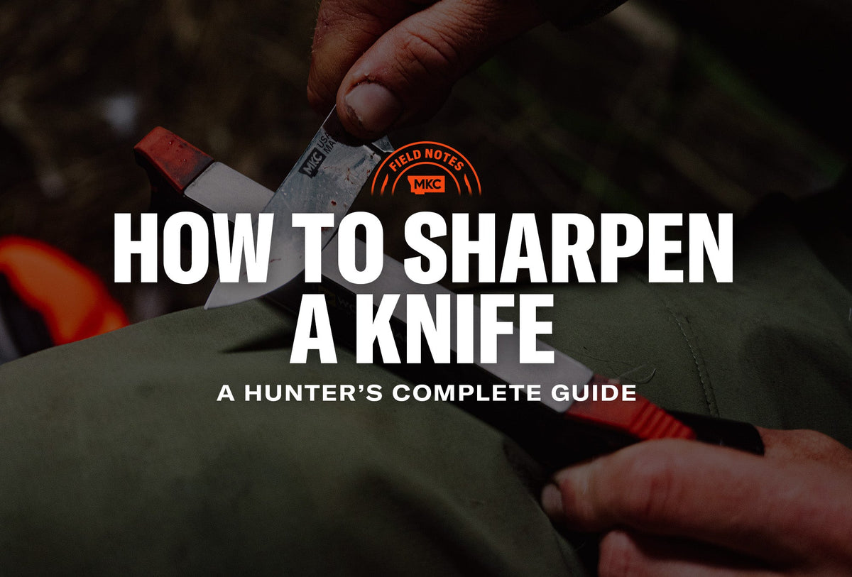 Hands sharpening an MKC knife on a field sharpener outdoors, with the blade resting on green fabric.