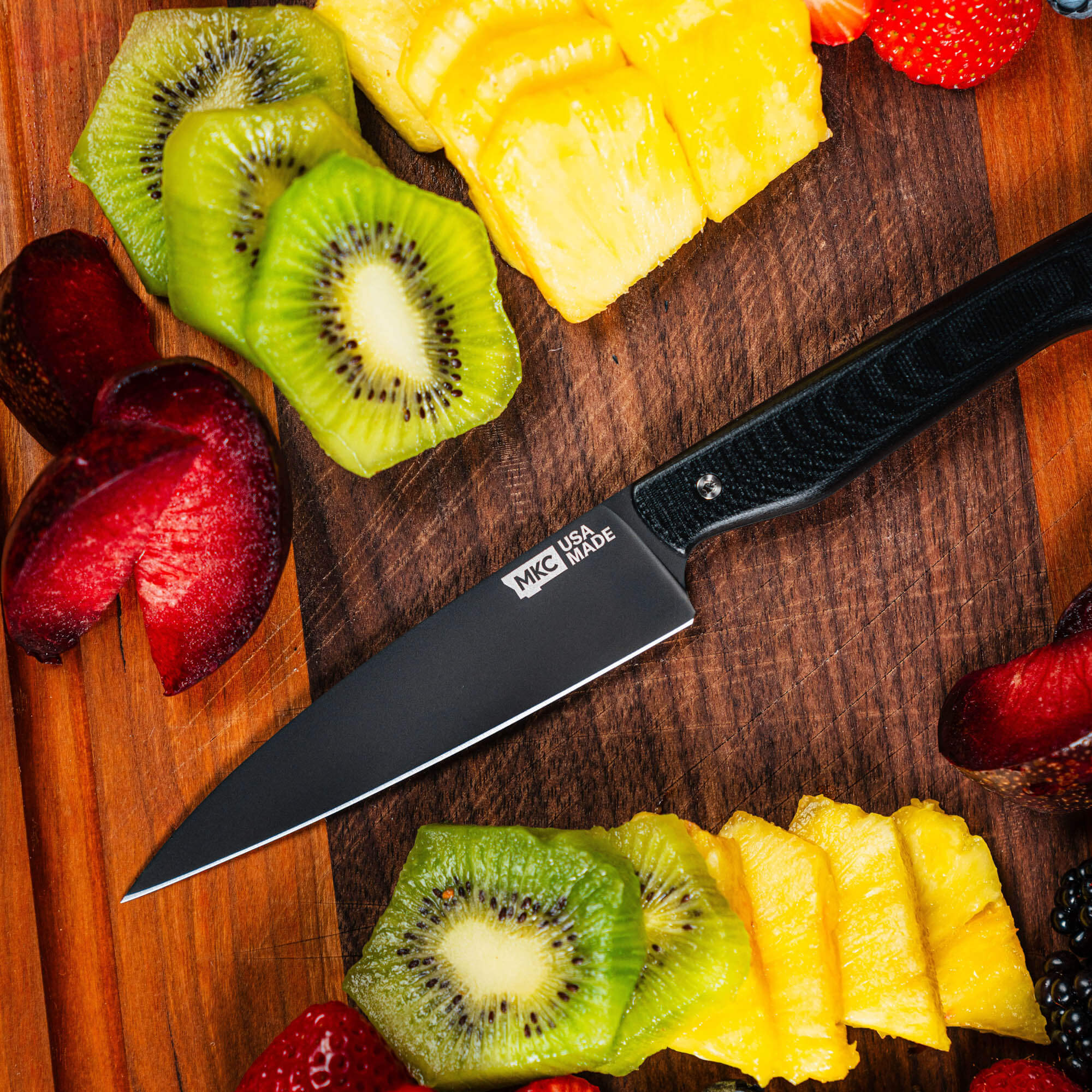 Montana Knife Company's Cutbank Paring Knife with a black handle, surrounded by sliced fruits on a wooden cutting board.