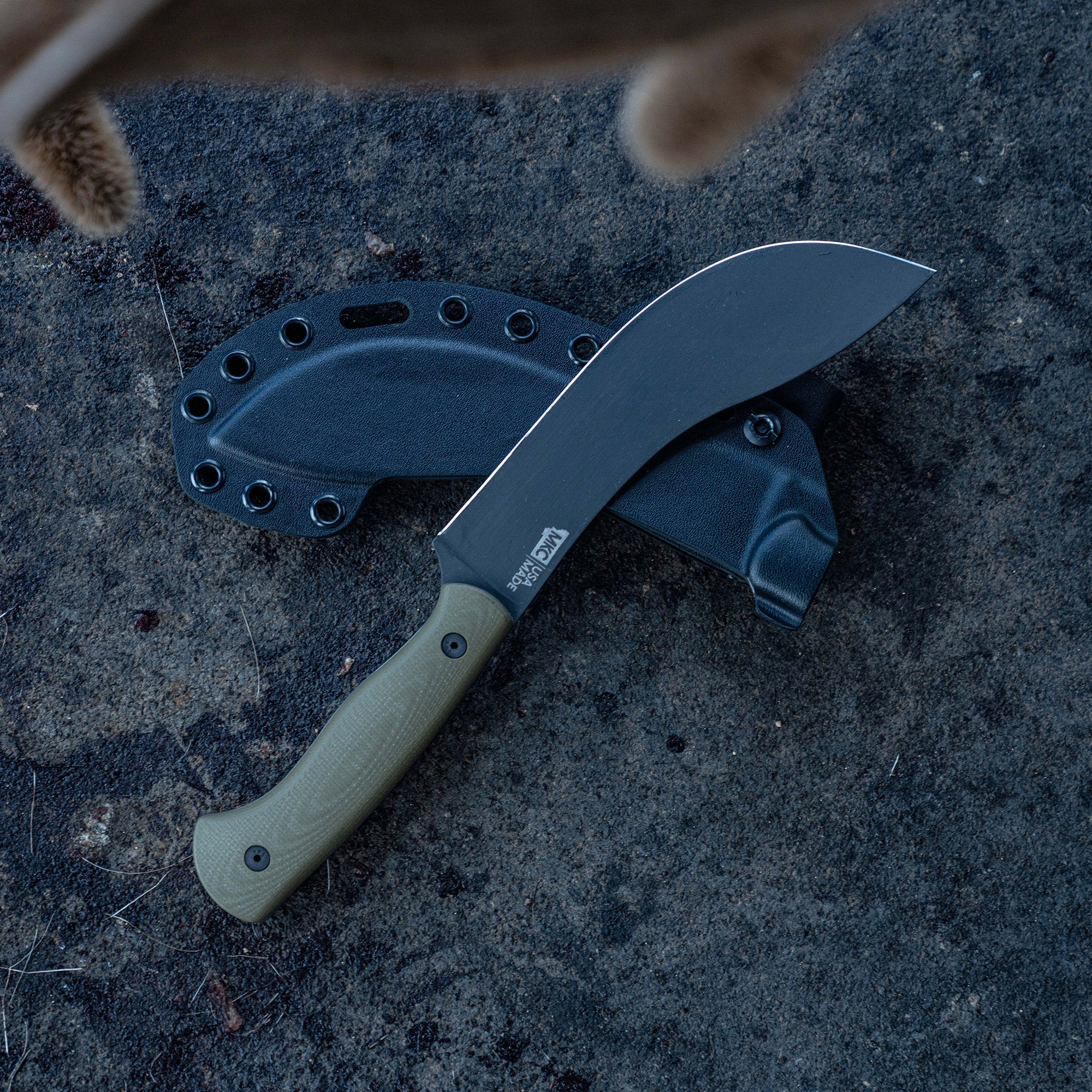 Alt text: "Beartooth Pro Skinning Blade with an olive green handle and black sheath displayed on a rocky surface. The blade features a sleek, curved design ideal for skinning, with the Beartooth logo visible on the blade."