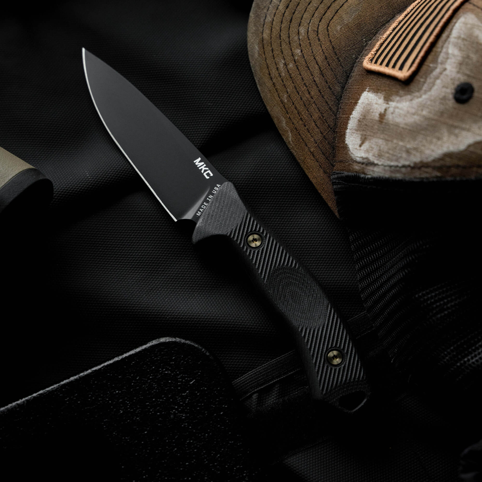 Montana Knife Company's TF24 knife features a sleek black blade and textured handle, set against a dark background.