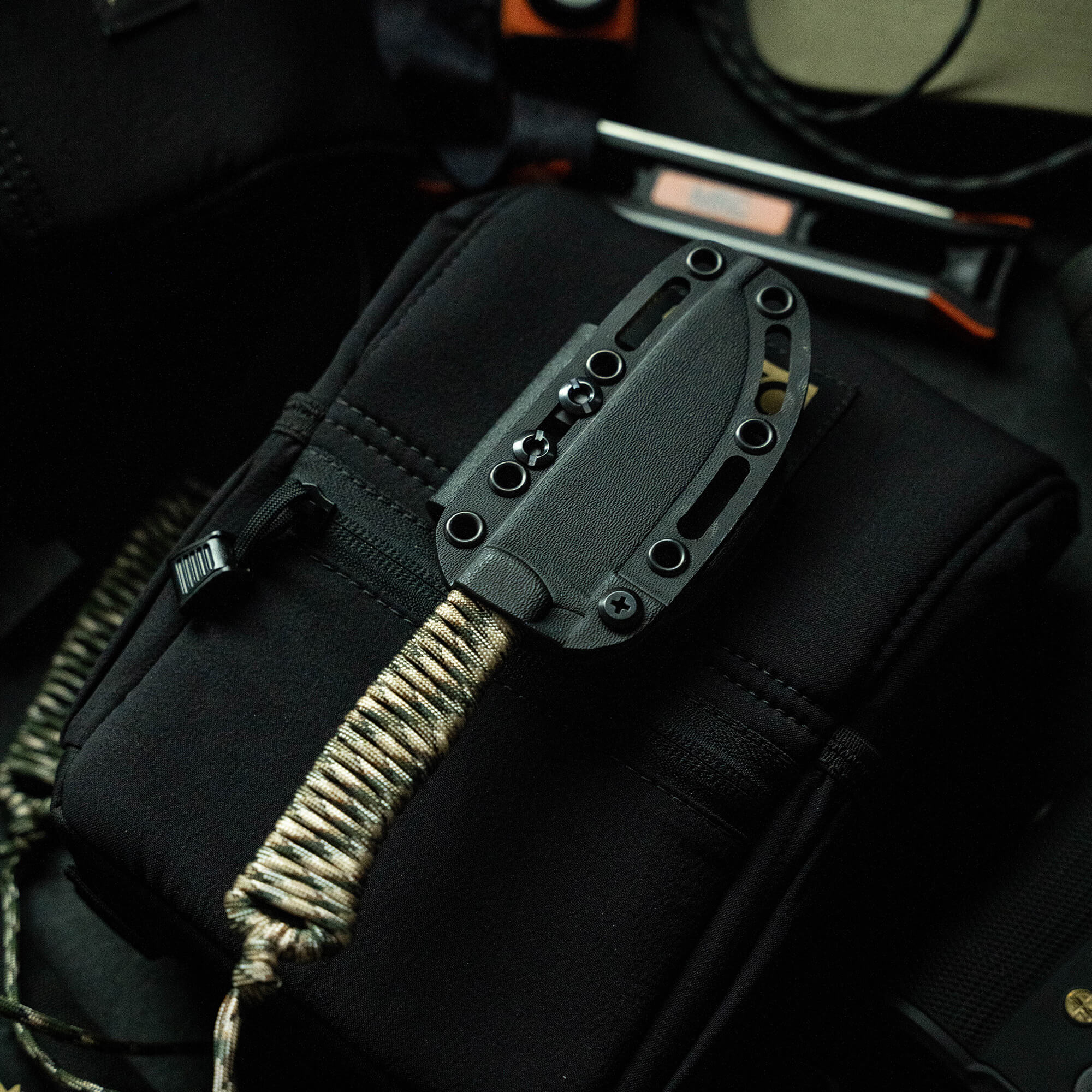 Alt text: Close-up of a tactical knife in a black sheath attached to a black backpack, featuring sturdy straps and outdoor gear around it, from the Wild Sheep Foundation Stoned Goat 2.0 Secret Drop collection, labeled as sold out.