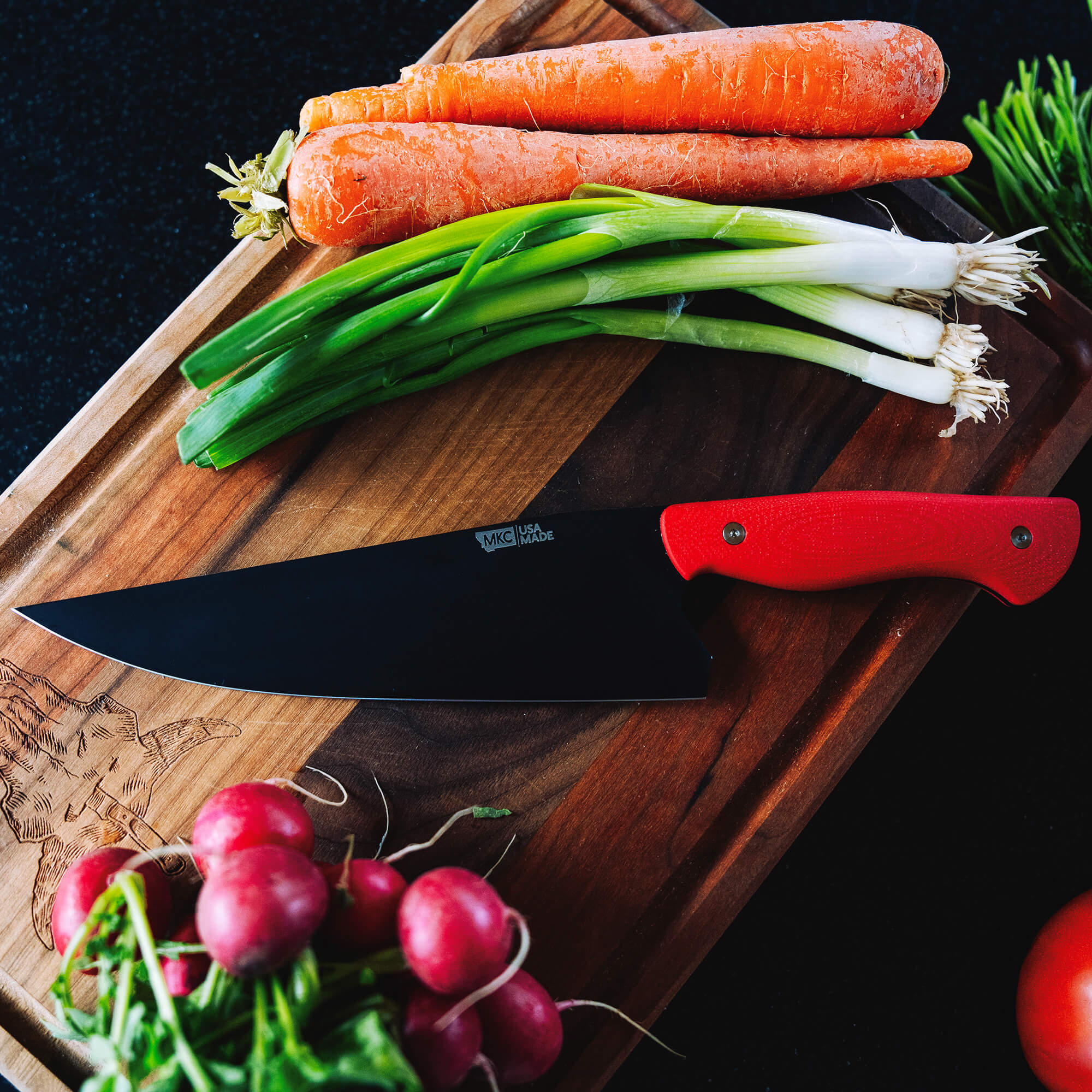 "BIGHORN Chef’s knife with a vibrant red handle, prominently displayed beside fresh carrots, green onions, and radishes on a wooden cutting board."