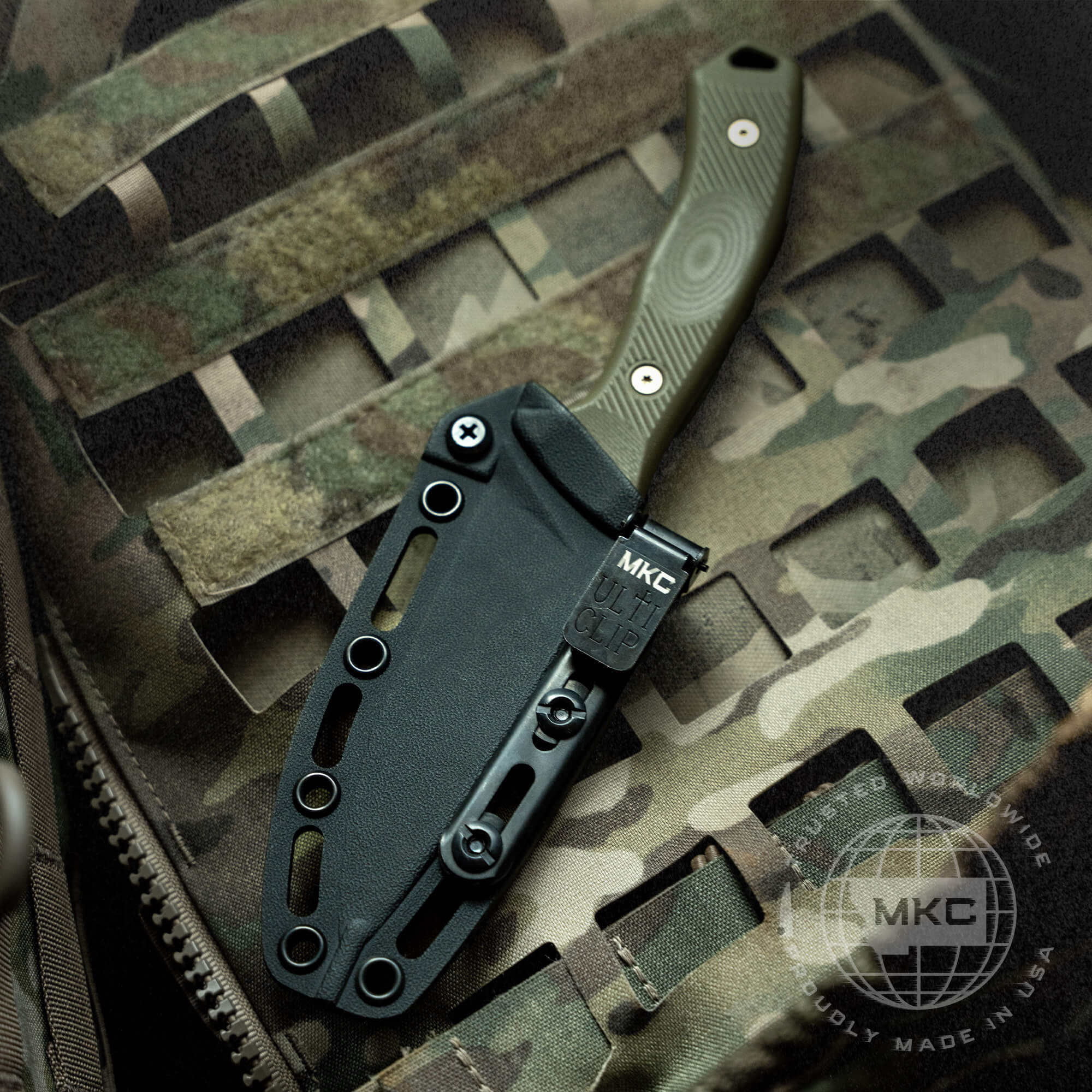 A black Kydex sheath holding a green handled knife, with a metal clip labeled "MKC" attached, positioned on a camouflaged background.
