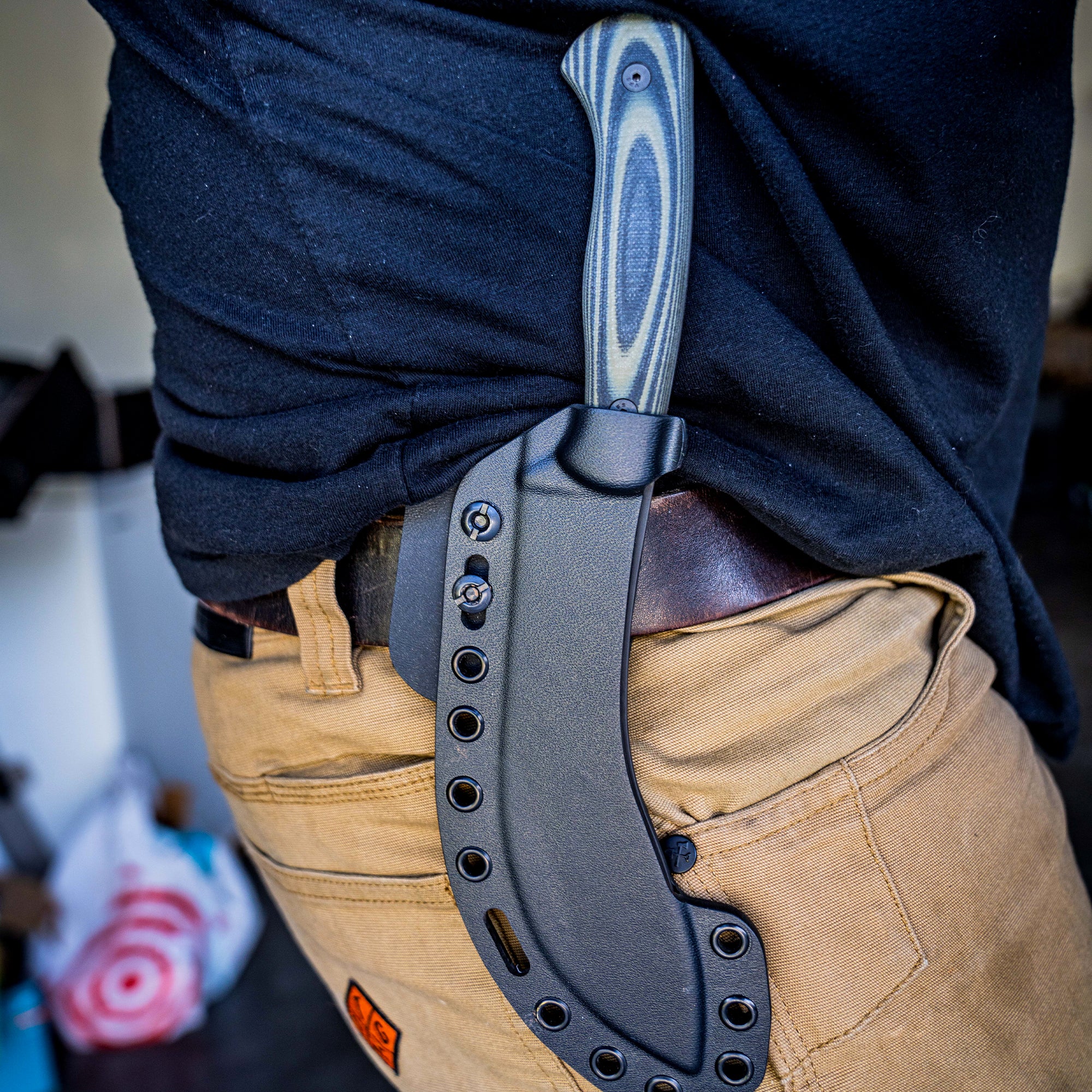 Alt text: "Close-up of a BEARTOOTH Pro Skinning Blade in green and black, attached to a black sheath secured to the belt of khaki pants, highlighting the knife's layered handle design and robust construction."
