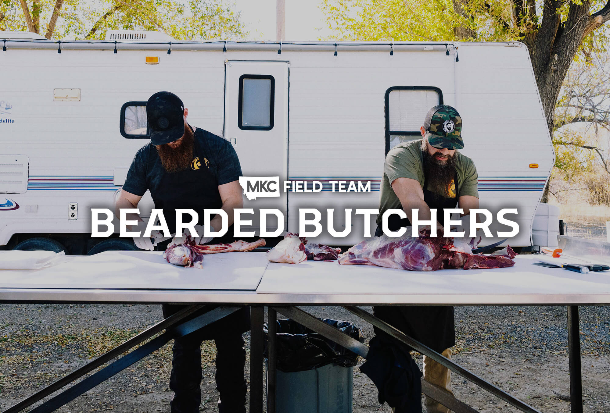 Brothers Seth and Scott Perkins, AKA the Bearded Butchers, smile while standing in front of hanging meats.