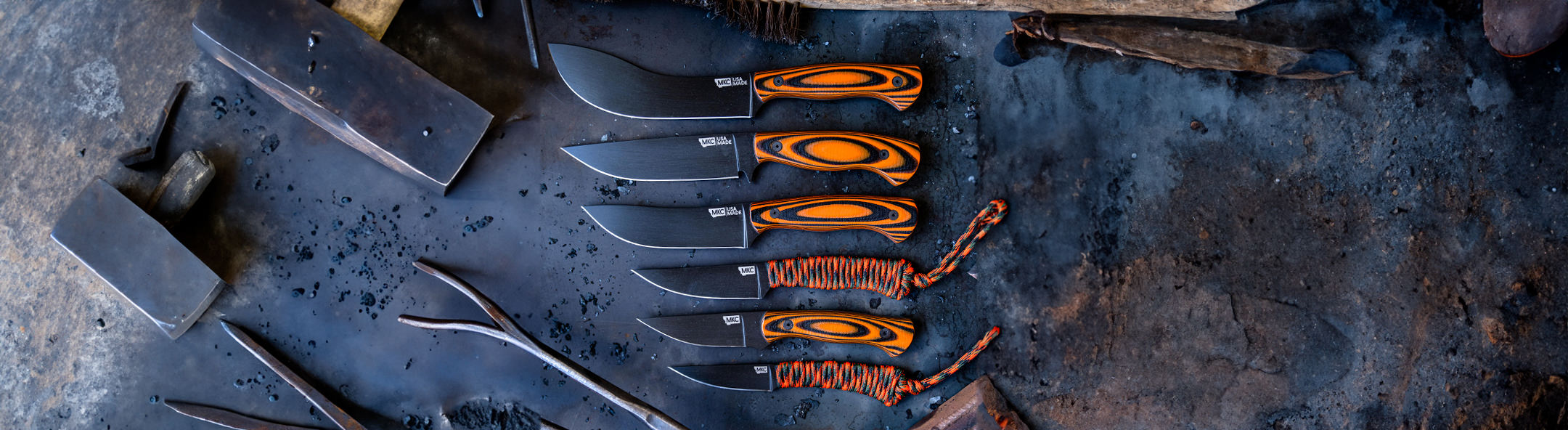 A collection of Montana Knife Company blades featuring black steel and orange handles, arranged on a textured surface.