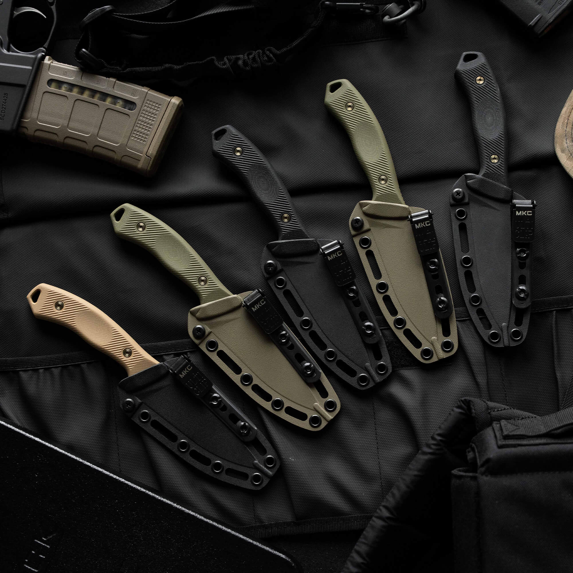 Five MTNTOUGH TF24 knives in various colors displayed on a tactical background, showcasing their durable sheaths and ergonomic grips.