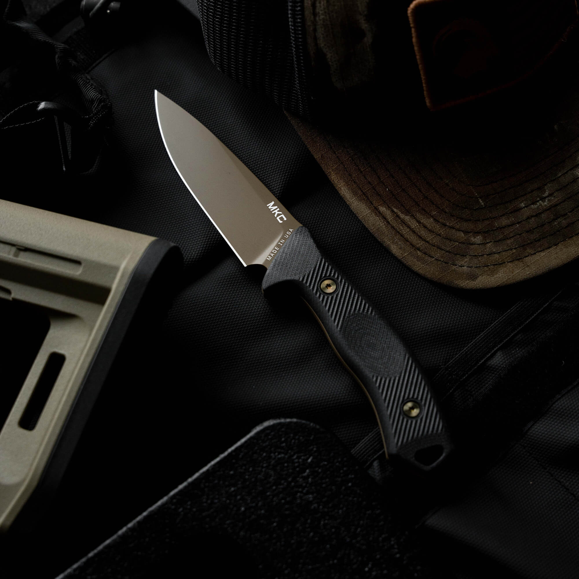 Montana Knife Company's TF24 knife displayed on a tactical background with a cap and gear, showcasing its rugged design.