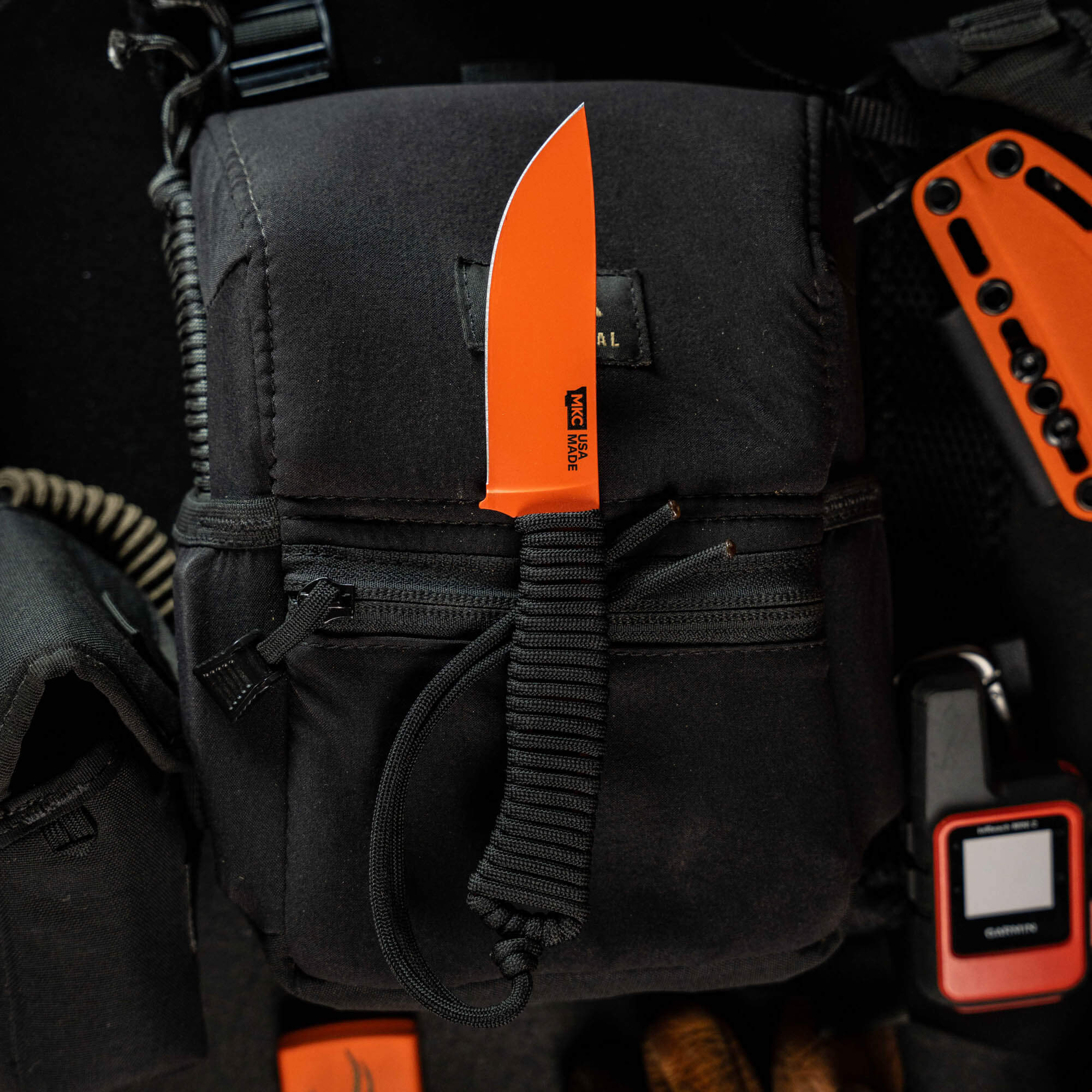Blaze orange Cerakote Stoned Goat 2.0 knife on a black tactical pouch, showcasing its durable design for outdoor use.