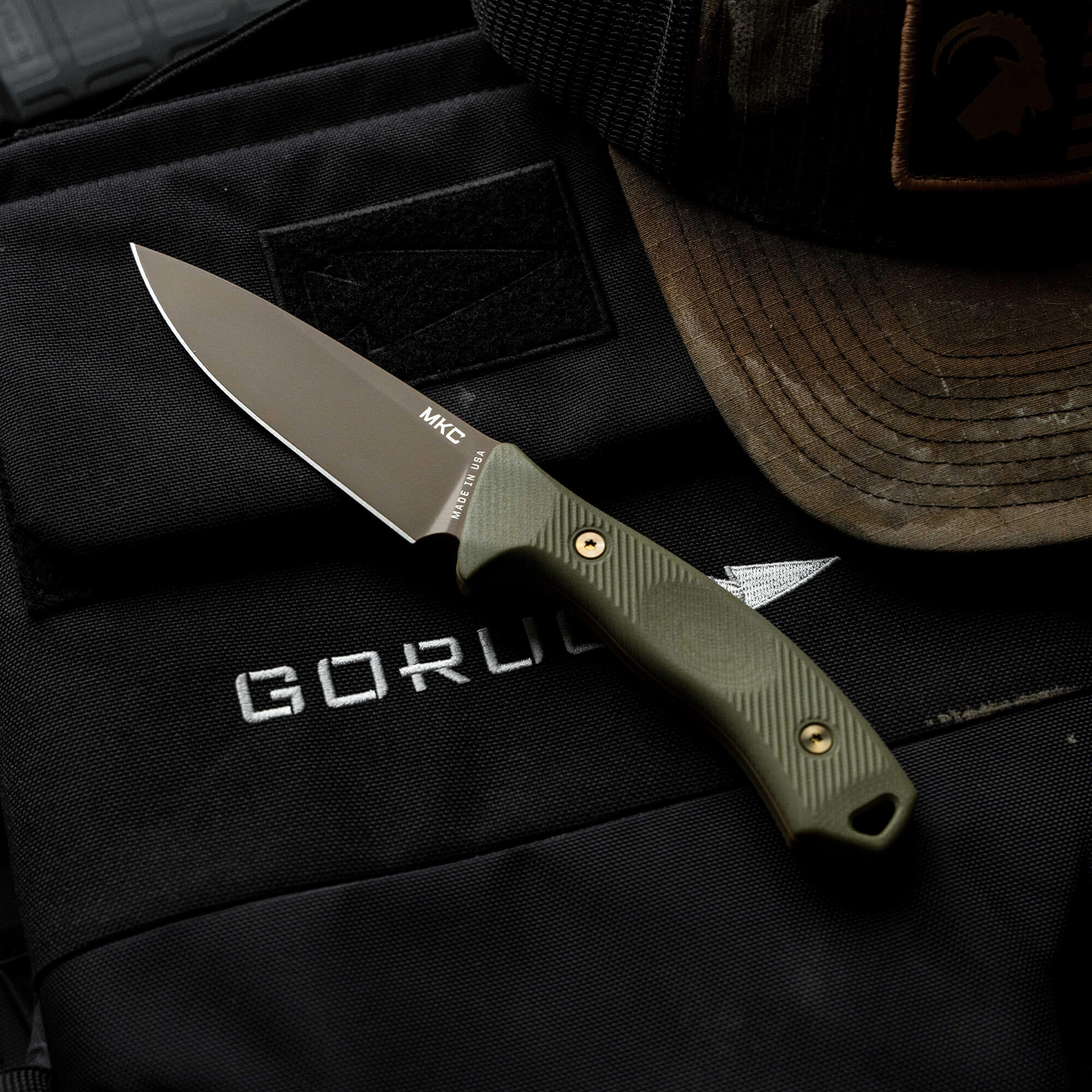 MTNTOUGH TF24 knife displayed on a tactical bag with a cap, showcasing its rugged design and functionality.