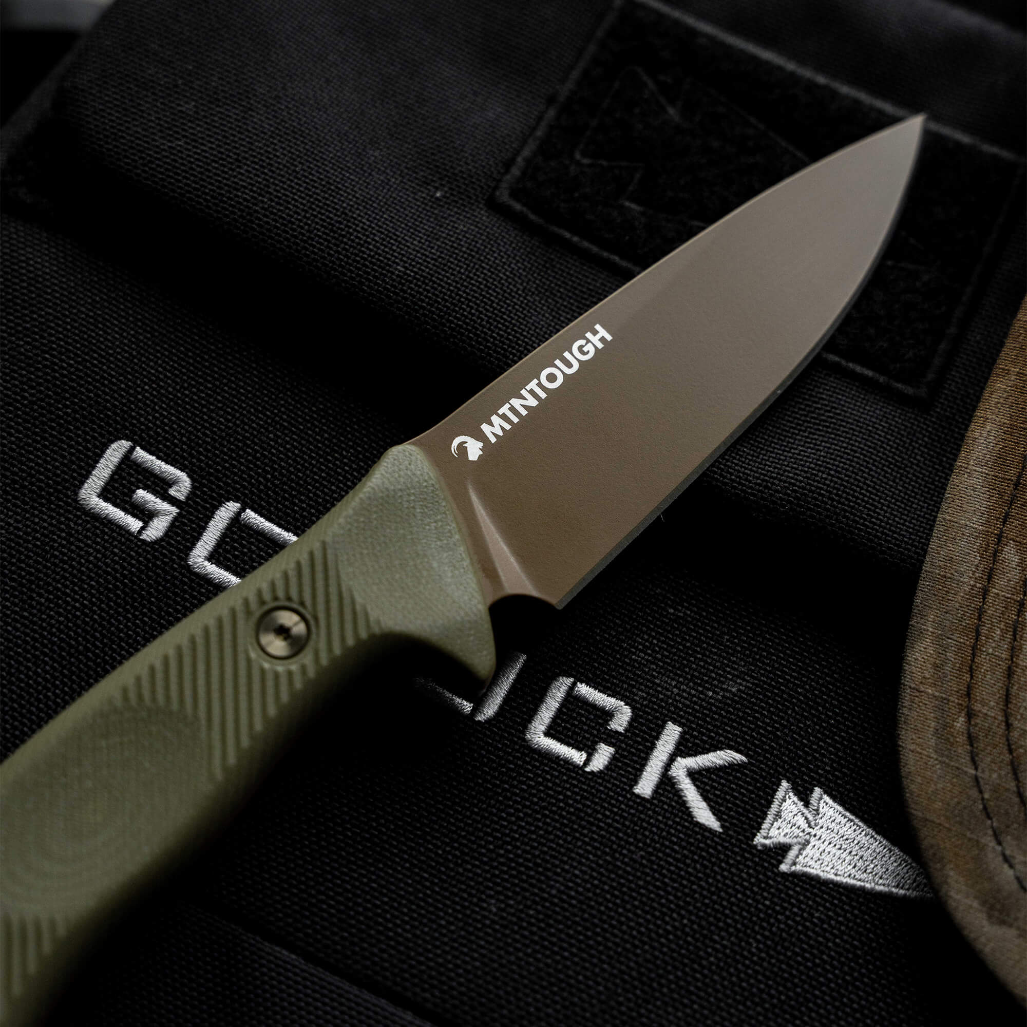 MTNTOUGH TF24 knife featuring a sleek blade and ergonomic green handle, resting on tactical gear.