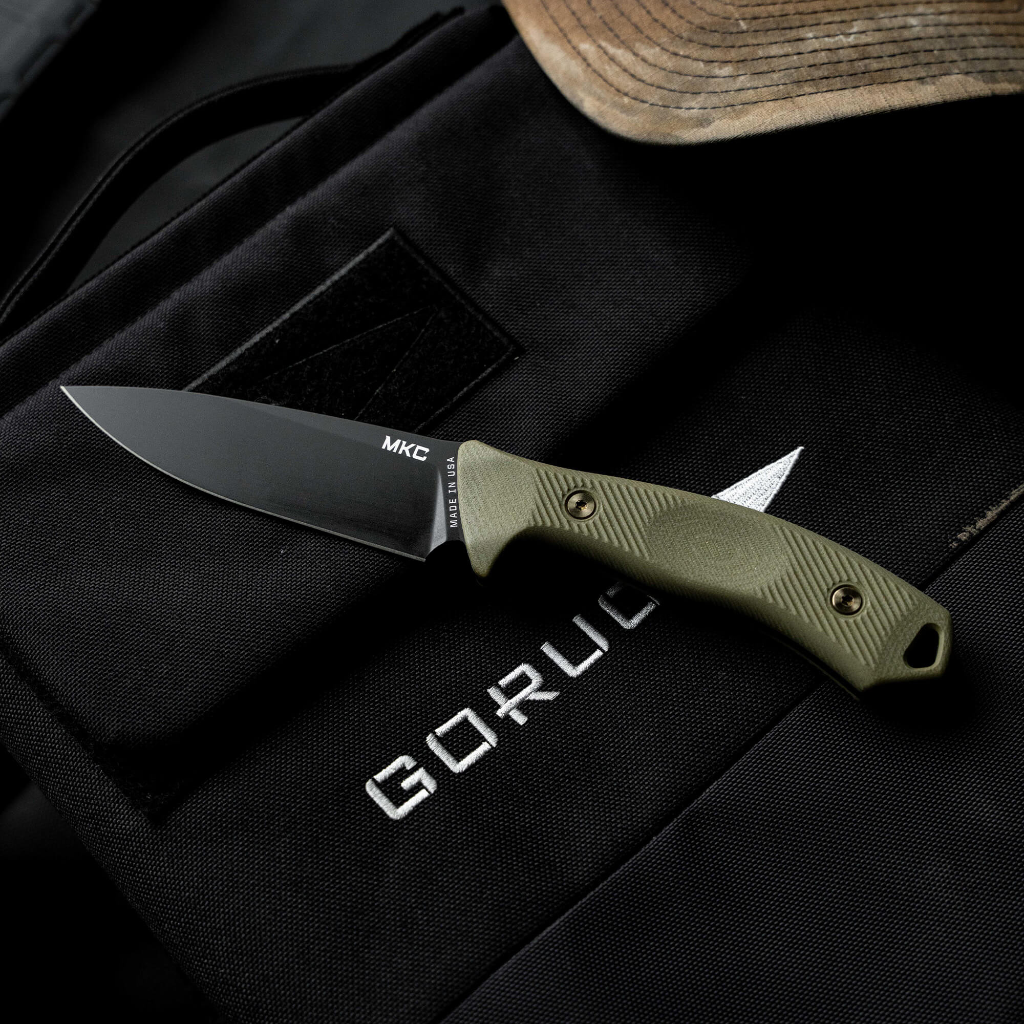 MTNTOUGH TF24 knife with a black blade and green textured handle, resting on a tactical bag.