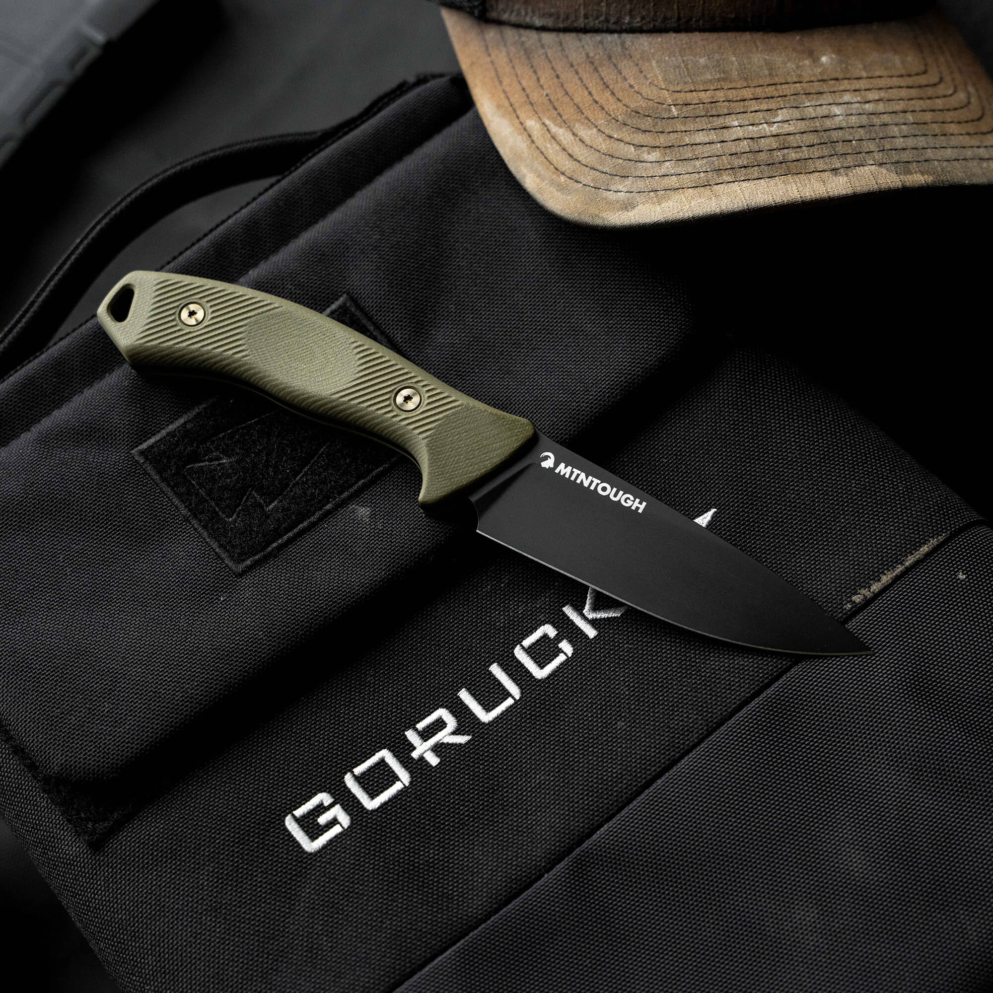 MTNTOUGH TF24 knife with a black blade and green handle resting on a tactical bag, showcasing rugged outdoor gear.