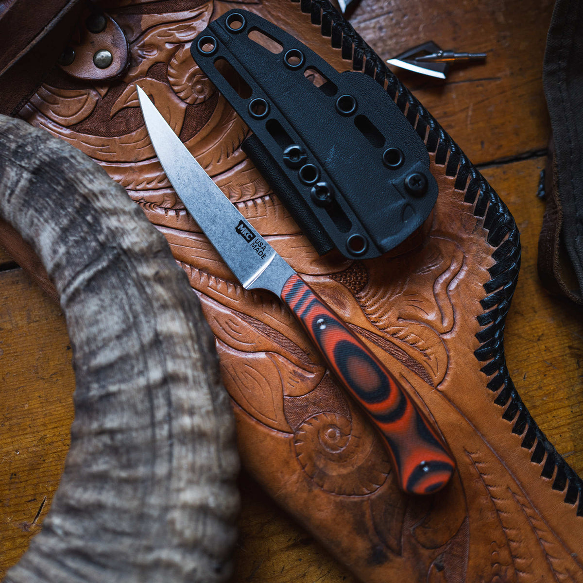 Orange and black field boning knife on a leather surface with a black sheath, showcasing its sharp blade and ergonomic handle.