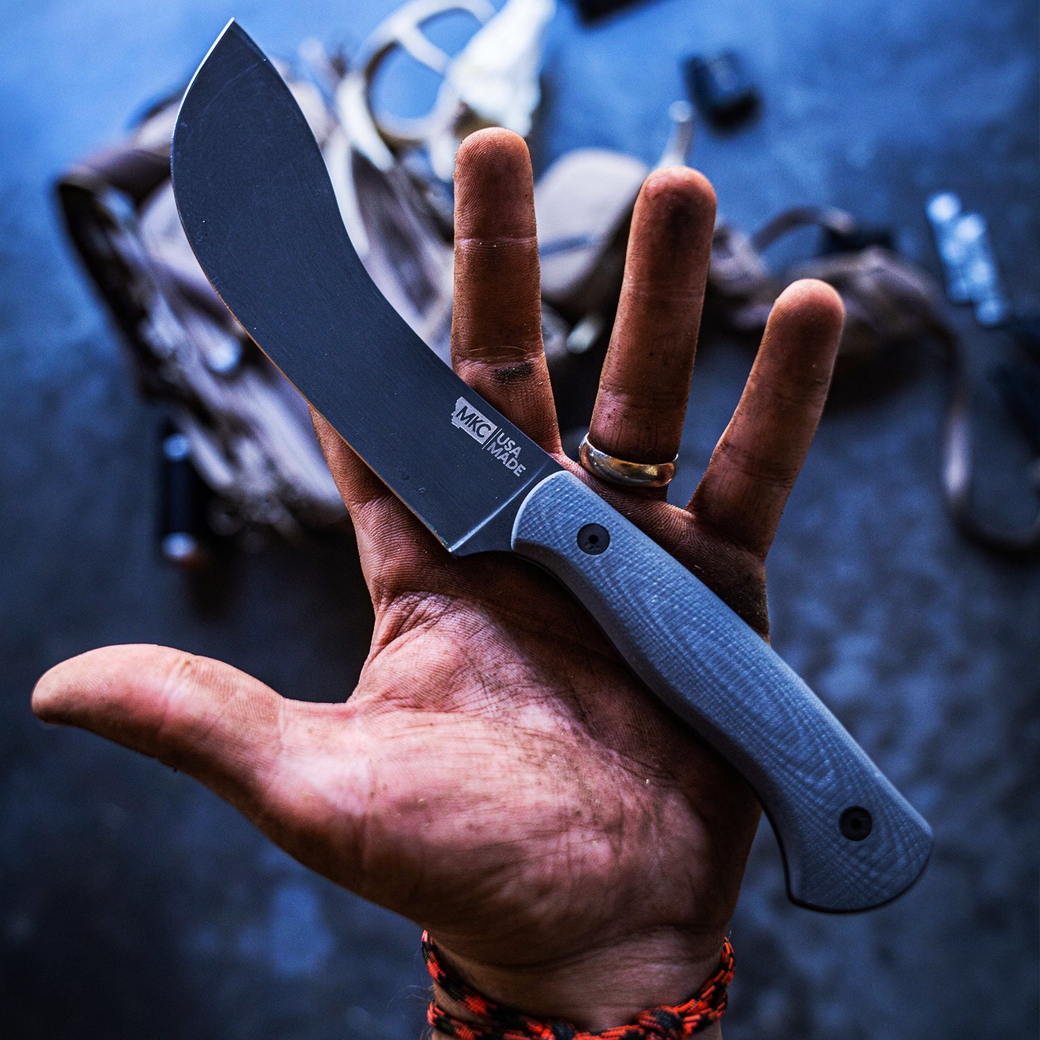 A close-up image of a grey BEARTOOTH Pro Skinning Blade held in a person's hand, showcasing its sleek and sturdy design, ideal for precise skinning tasks. The workshop background subtly hints at the blade's professional use.